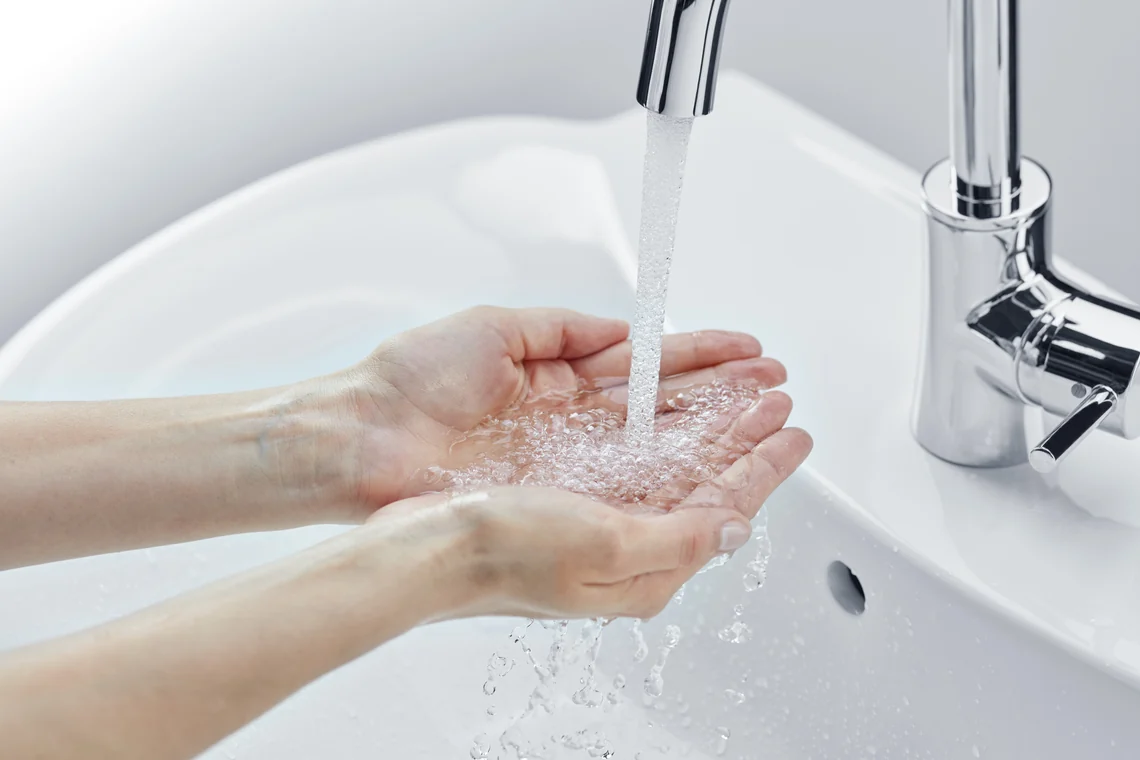 Hände unter fließendem Wasser an einer Waschtischarmatur